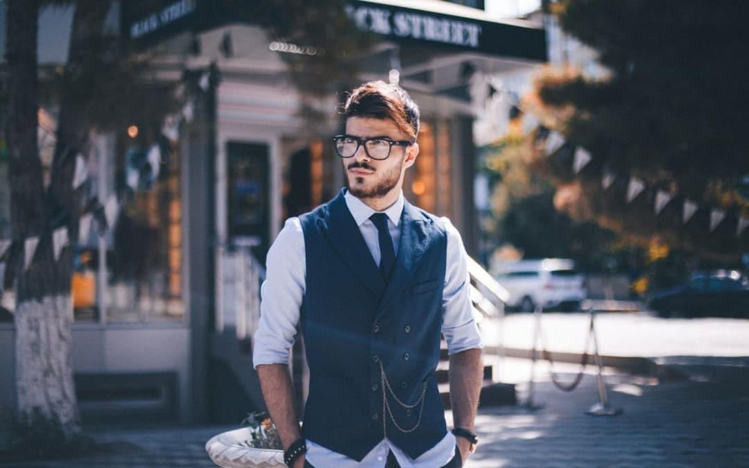 Stylish man with glasses, beard, and blue vest in urban setting