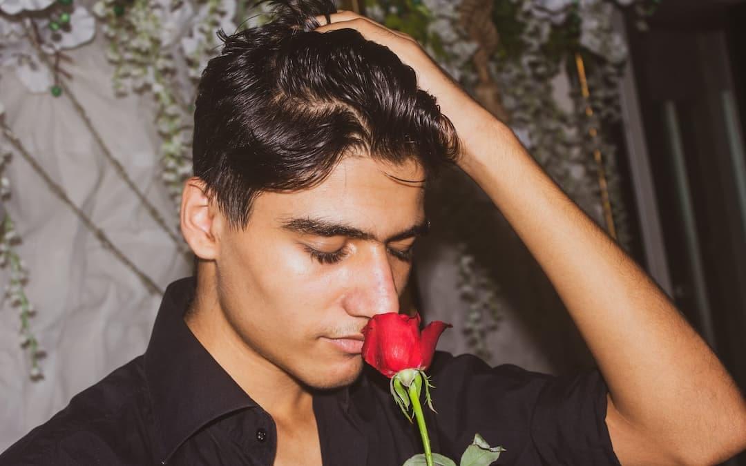 Young man with black hair smelling a red rose